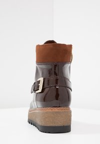 Hnědé lakované kožené kotníkové boty s hnědým semišovým manžetou, dekorační přezkou, texturovanou podrážkou a středně silným platformovým podpatkem.