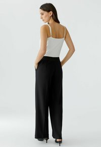 White spaghetti strap top paired with wide-leg black pants featuring a contrasting waistband. Smooth fabric and sleek silhouette.