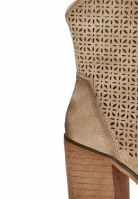 Botín de ante beige con diseño perforado, tacón de madera apilado, superficie texturizada y silueta superior curvada.