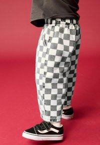 Pantalons à damier noir et blanc avec une taille élastique et des poches latérales, associés à des baskets noires avec des accents blancs.