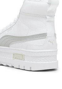 Sneaker alta bianca in pelle sintetica, con accenti grigi, suola testurizzata e logo prominente sul tallone. Presenta una linguetta e un collare imbottiti.