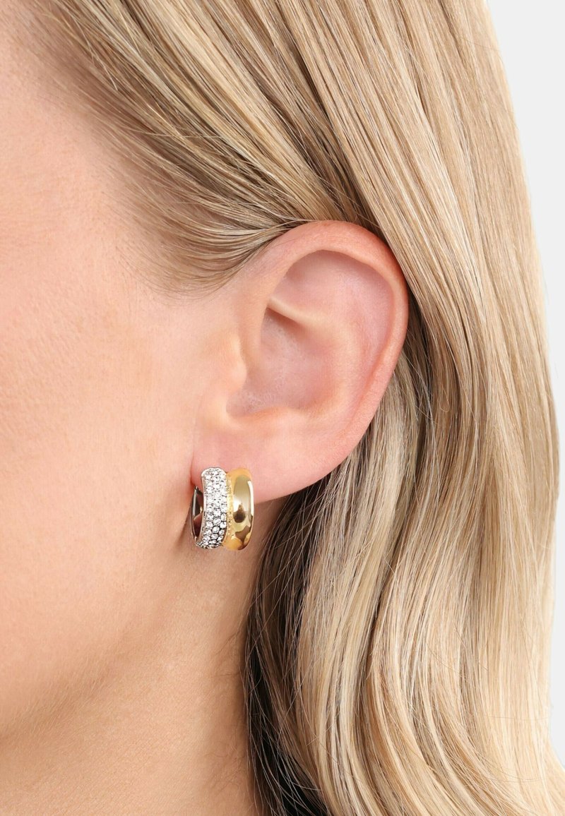 Orecchini a cerchio in oro e argento, caratterizzati da una fascia d'oro liscia e una fascia d'argento arricchita con strass trasparenti, mostrati in evidenza contro i capelli.