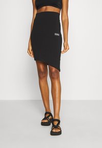 Svart jerseykjol med en åtsittande midja, prydd med en PUMA-logotyp. Designad med en asymmetrisk nederkant och mjukt tyg.