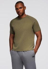 Olivengrøn t-shirt med korteærmer, rund halsudskæring og raglanærmer, parret med grå sweatpants. Glat tekstur, afslappet design.