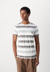 Camiseta a rayas en blanco, con rayas horizontales negras y verde menta, cuello redondo, mangas cortas y un pequeño bolsillo frontal con acento de logo.