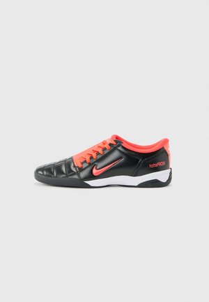 Zapato de fútbol Nike Total 90 en negro y rojo con cordones, diseño de puntera cosida y suela blanca y negra, visto de lado sobre un fondo liso.
