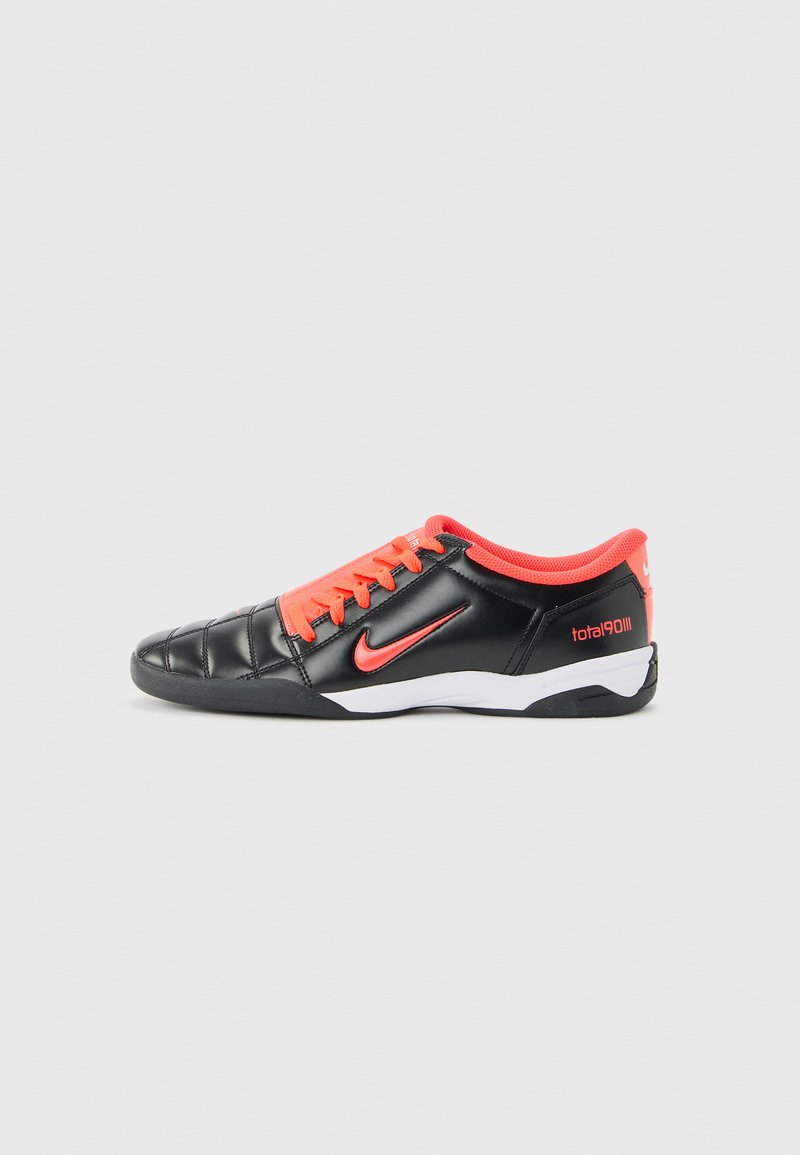 Fekete és piros Nike Total 90 futballcipő fűzőkkel, varrott orrkialakítással és fehér-fekete talppal, oldalról egy egyszerű háttér előtt ábrázolva.