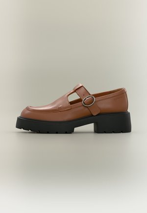 Bruine leren loafer met uitneemontwerp, zilverkleurige gesp, en dikke zwarte zool, zijaanzicht op een neutrale achtergrond.