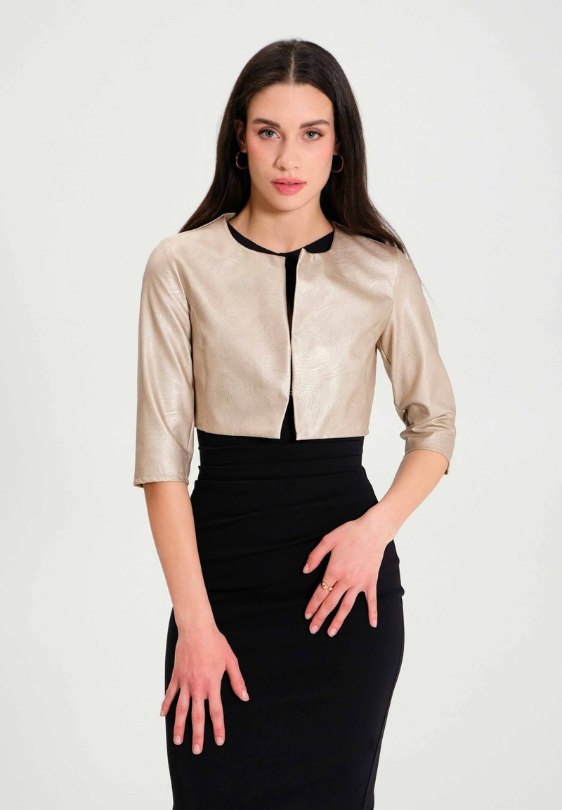 Metallic gold cropped jacket with three-quarter sleeves, round neckline, and black accents, worn over a form-fitting black dress.