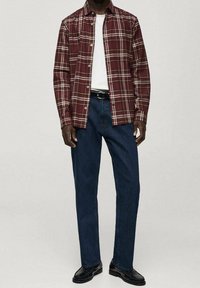 Camisa de cuadros en burdeos y crema, diseño de botones; combinada con jeans azul oscuro y zapatos negros, creando un atuendo informal.