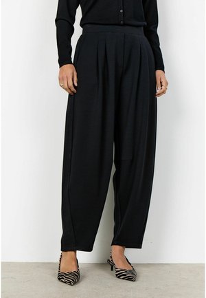 Czarne plisowane spodnie wykonane z miękkiego materiału, z wysokim pasem i szerokimi nogawkami. Zestawione z czarno-białymi butami na obcasie w paski.