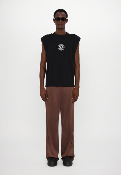 T-shirt preta sem mangas com um gráfico circular, calças largas castanhas e sapatos plataforma pretos. Textura suave, design minimalista.