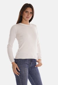 Maglione a maniche lunghe di un crema chiaro in un design aderente con scollatura rotonda e polsini a coste, abbinato a jeans aderenti di un blu scuro.