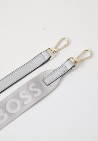 Cintura in pelle grigia con una sezione intessuta beige che presenta la scritta "BOSS" in lettere gonfiate e clip in metallo dorato ad entrambe le estremità.
