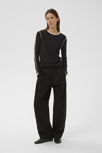 Mustast pikkade varrukatega topp kreemika ääristusega, kantud koos lõdvestunud mustade pükstega. Mõlemal rõival on sile tekstuur ja minimalistlik disain.