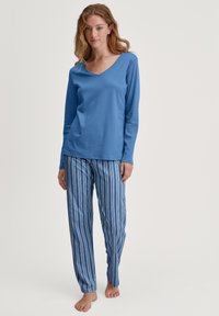 Blauw langemouwen top met een v-hals, gecombineerd met blauw-witte gestreepte pyjamabroek. Zachte stof, ontspannen pasvorm, blootvoets.