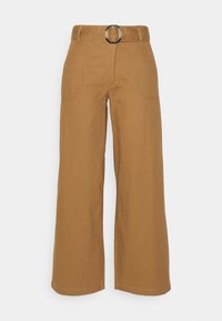 Breda byxor i tanfärgad bomull med ett framfäste som har en silverfärgad cirkulär spänne och två framfickor. Slät textur och rak nederkant.