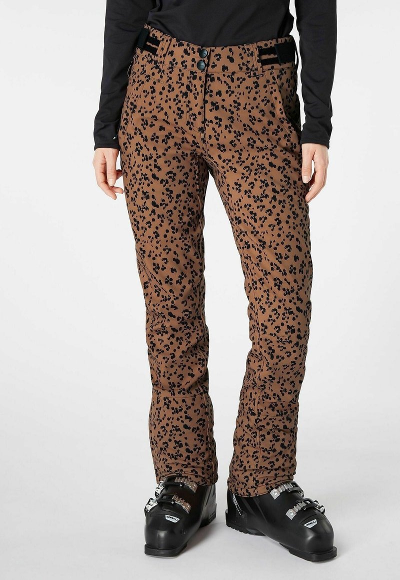 Pantalon de ski marron slim fit avec des taches léopard noires, porté avec des bottes de ski noires et un haut noir à manches longues.