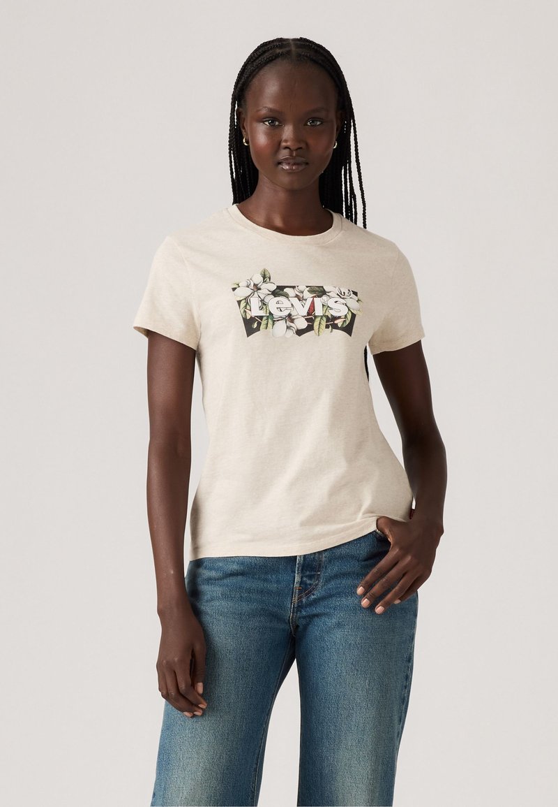 T-shirt en coton beige avec un graphique de logo floral Levi's, manches courtes, col rond et coupe ajustée. Porté avec un jean bleu.