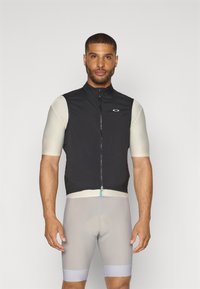Gilet de cyclisme noir avec un col haut et une fermeture éclair à l'avant, associé à un short gris clair avec des accents bleus et un rembourrage au niveau de l'assise.
