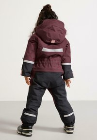 Tweedelige kinder winterset, bordeauxrood en zwart, met reflecterende strepen, verstelbare capuchon en elastische manchetten, ontworpen voor buitengebruik.