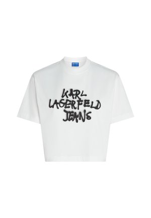Fehér, pamutból készült, cropped póló, melynek elején fekete spray-rajzolt szöveg található: "KARL LAGERFELD JEANS" laza betűtípussal. Rövid ujjú, kerek nyakkivágású.