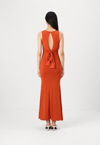 Robe longue et ajustée en orange rouille, sans manches, avec un dos en trou de serrure et un détail de taille nouée. Tissu lisse, s'évase à l'ourlet.