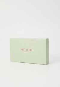 Vihreä pahvilaatikko kiiltävässä pinnassa. Edessä on "TED BAKER LONDON" punaisella kirjasimella. Suorakulmainen muoto, jossa on puhtaat reunat.