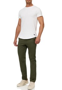 Camisa blanca de manga corta con escote redondo, combinada con pantalones ajustados verde oliva y zapatillas beige. Diseño simple y casual.