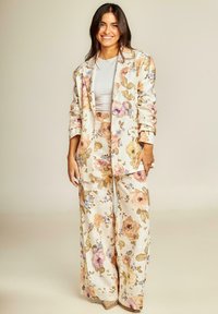 Ensemble floral deux pièces en beige clair, comprenant un blazer et un pantalon large avec des motifs floraux pastels. Tissu doux avec une coupe décontractée.