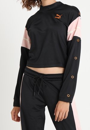 Crop top Puma manches longues noir et rose avec œillets orange sur les manches, associé à un pantalon noir à cordon de serrage avec des bandes latérales roses.