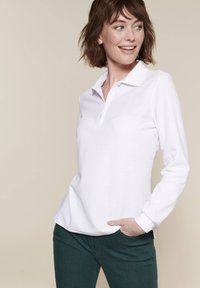 Polo shirt bianco a maniche lunghe con colletto e tre bottoni. Materiale morbido. Abbinato a pantaloni verde scuro. Design semplice e classico.