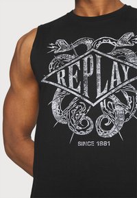 Camiseta sin mangas negra con un diseño gráfico de serpientes y la palabra "REPLAY" en texto blanco desgastado. Material de algodón, cuello redondo.