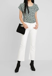 Světle zelený top s krátkým rukávem a černým tečkovaným vzorem, spárovaný s bílými zvonovými džínami. Černá semišová kabelka a špičaté kotníkové boty.