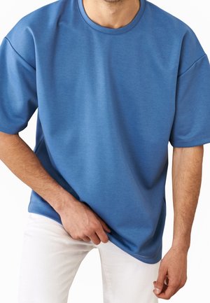 Blå kortærmet t-shirt i et blødt, tekstureret stof med rund hals og afslappet pasform, kombineret med hvide bukser.