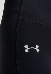 Černé legíny vyrobené z elastického, hladkého materiálu, s plochými švy a výrazným stříbrným logem na levé stehně.