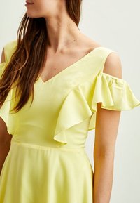 Yellow dress with a V-neckline and off-the-shoulder flutter sleeves; smooth texture and flowing fabric create a feminine silhouette.
