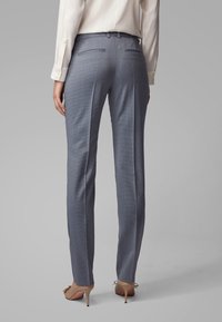 Grijze op maat gemaakte broek met een subtiele ruitenpatroon. Heeft een aansluitende taille, twee achterzakken en smalle pijpen. Gecombineerd met beige hakken.