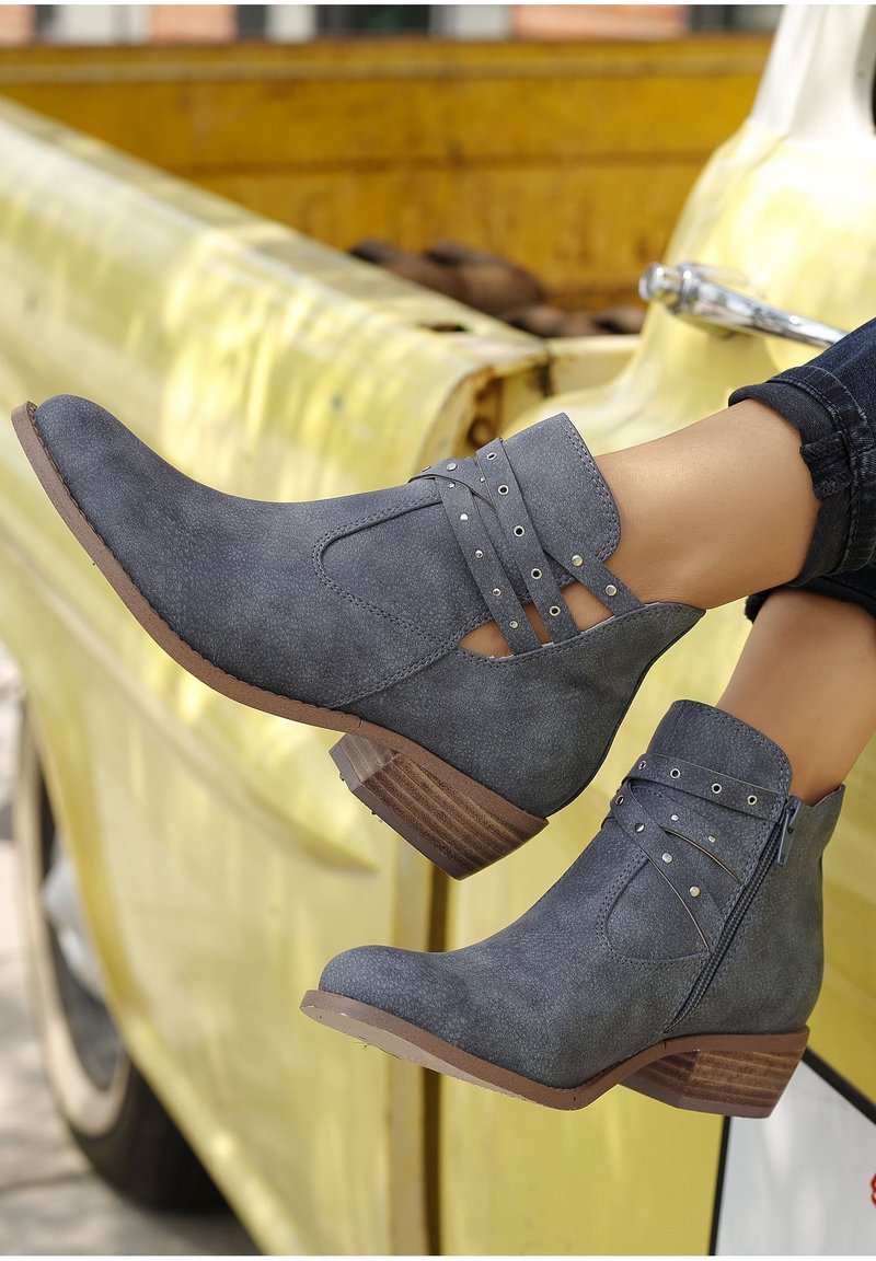 Bottines grises à talon empilé, avec un design découpé et des sangles décoratives, fabriquées dans un matériau texturé, sur un fond jaune.