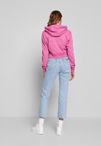 Avskuren rosa hoodie med dragsko på huvan, i kombination med ljusblå högmidjade jeans. Vita sneakers fulländar outfiten.