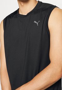 Maglietta sportiva nera senza maniche realizzata in tessuto leggero, con un sottile logo Puma grigio sul lato sinistro superiore. Texture liscia, vestibilità atletica.