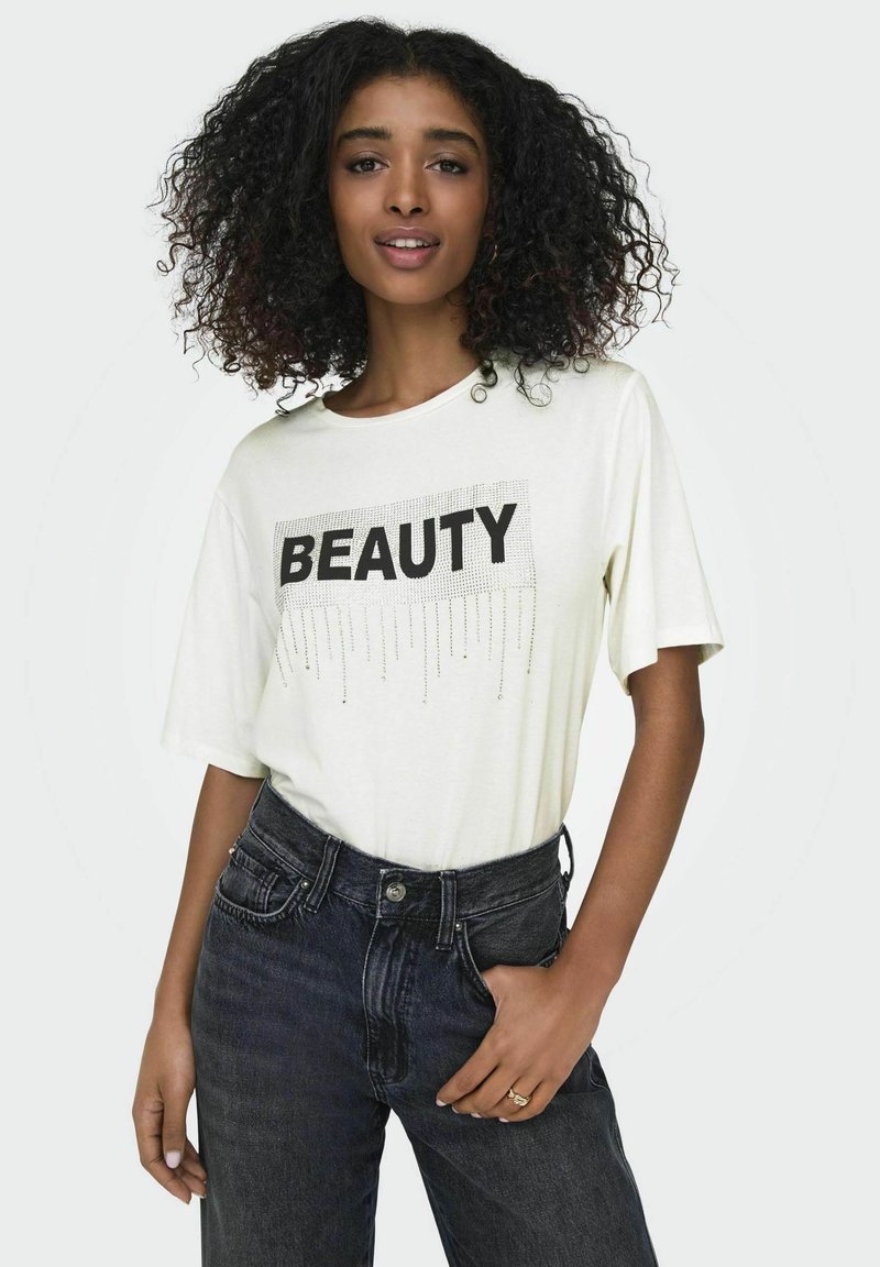 Witte t-shirt met korte mouwen, met het woord "BEAUTY" in zwarte druk en decoratieve versieringen. Gemaakt met een donkere, hoge taille jeans.