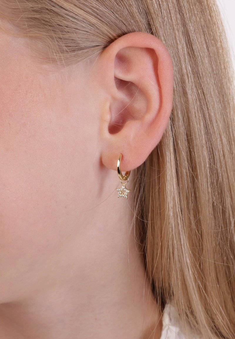 Gold hoop earring with a star charm, featuring a shiny surface and a small, clear stone accent. Worn on the lobe, close-up view.