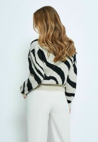 Maglione a maglia di colore chiaro con strisce zebra nere, finitura testurizzata, orlo a coste e polsini aderenti. Abbinato a pantaloni di colore chiaro.
