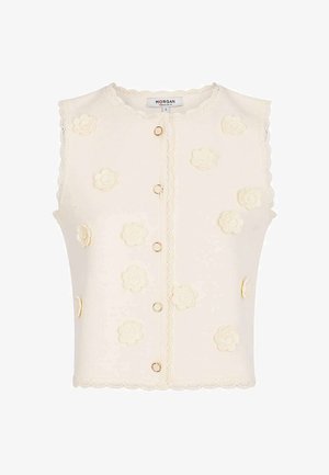 Cardigan sans manches crème avec bords festonnés, fermetures à boutons anneaux dorés et appliqués floraux 3D sur le devant et les côtés.
