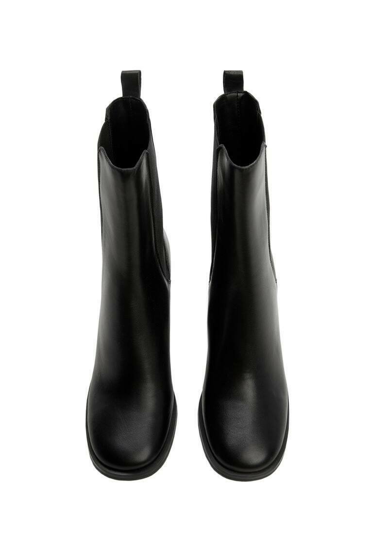 Botas de tobillo negras hechas de cuero suave, con una silueta esbelta, puntera redondeada y una lengüeta en la parte trasera para facilitar su uso.