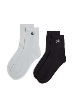 Chaussettes en coton noires et grises avec des bord-côtes, présentant un petit logo noir sur chaque chaussette. Texture lisse, longueur standard de type mi-mollet.