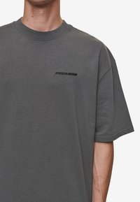 Graues Baumwoll-T-Shirt mit Rundhalsausschnitt und kurzen Ärmeln. Mit schwarzem "PEGADOR"-Schriftzug auf der Brust. Glatte Textur, lässige Passform.