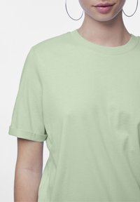 T-shirt in cotone verde chiaro con collo a giro classico, maniche corte arrotolate e una consistenza liscia. Senza patterns o hardware visibile.