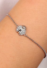 Bracciale argento con design centrale a chiusura, arricchito da brillanti accenti in zirconia cubica e una delicata catena, il tutto su uno sfondo color carne.